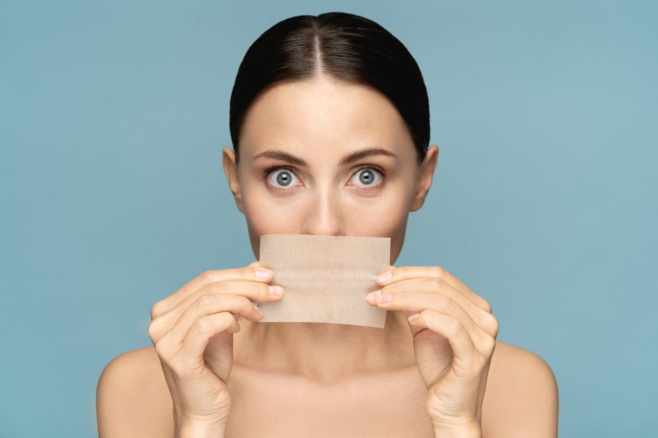 Woman with natural face makeup, holding facial oil blotting paper. Oil absorbing tissue, skin care