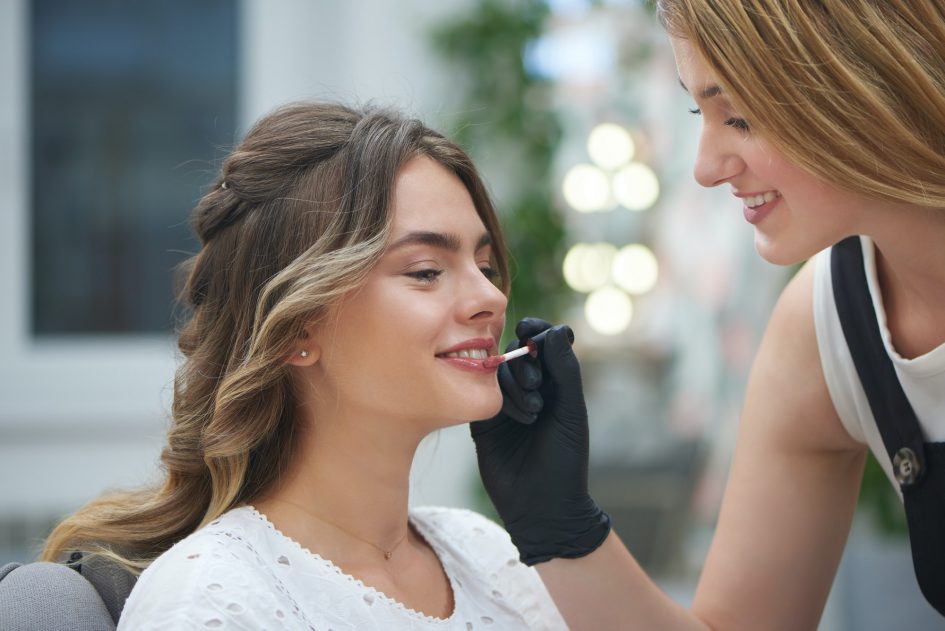 Makeup artist applying lip gloss in beauty salon