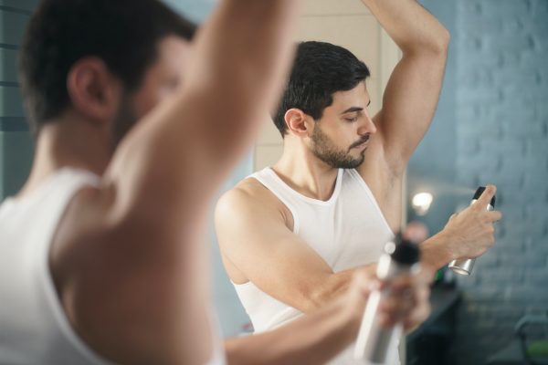 Man Using Spray Deodorant On Underarm For Bad Smell