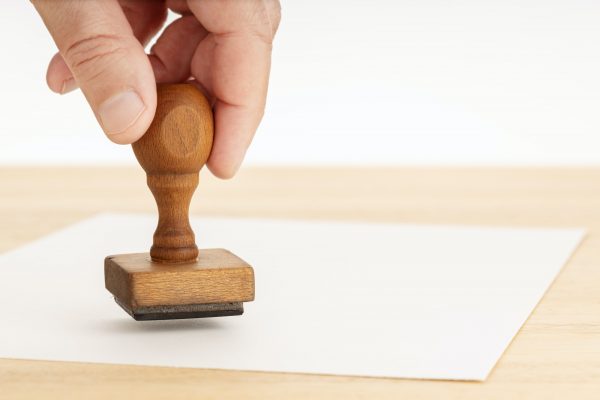 Hand holding a Rubber stamp and blank paper on wooden table